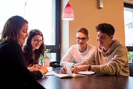Vier Schülerinnen und Schüler sitzen an einem Tisch und besprechen eine Gruppenaufgabe.