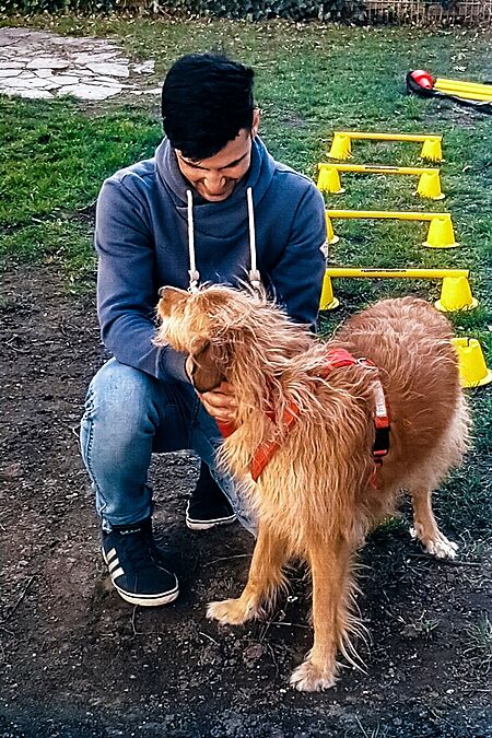 Der Jugendliche Abdullah spielt mit der Hündin Trulla im Park. Er sitzt in der Hocke, um mit der Hündin spielen zu können.